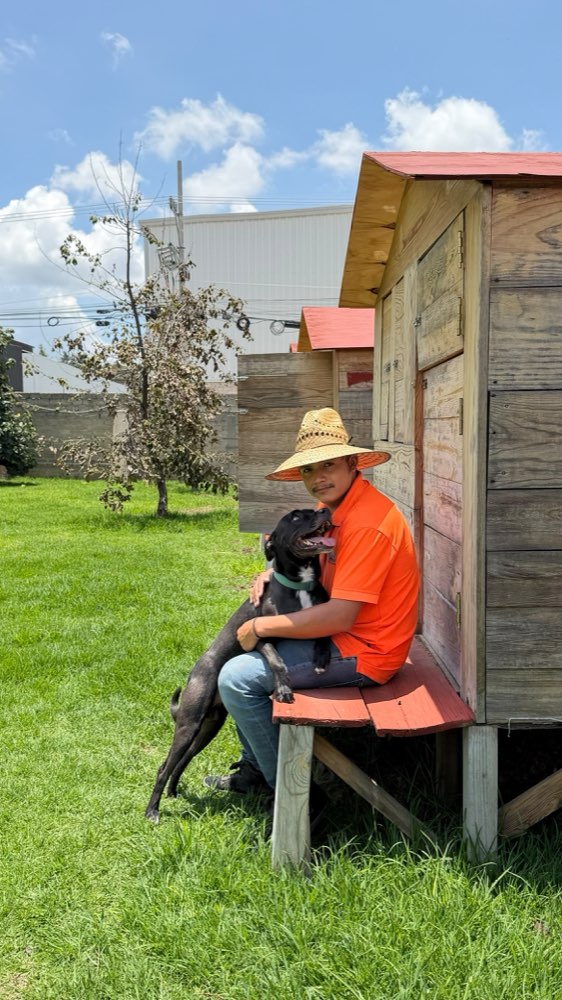 Cuidador abrazando a un perrito negro sentado en el porche de su casita